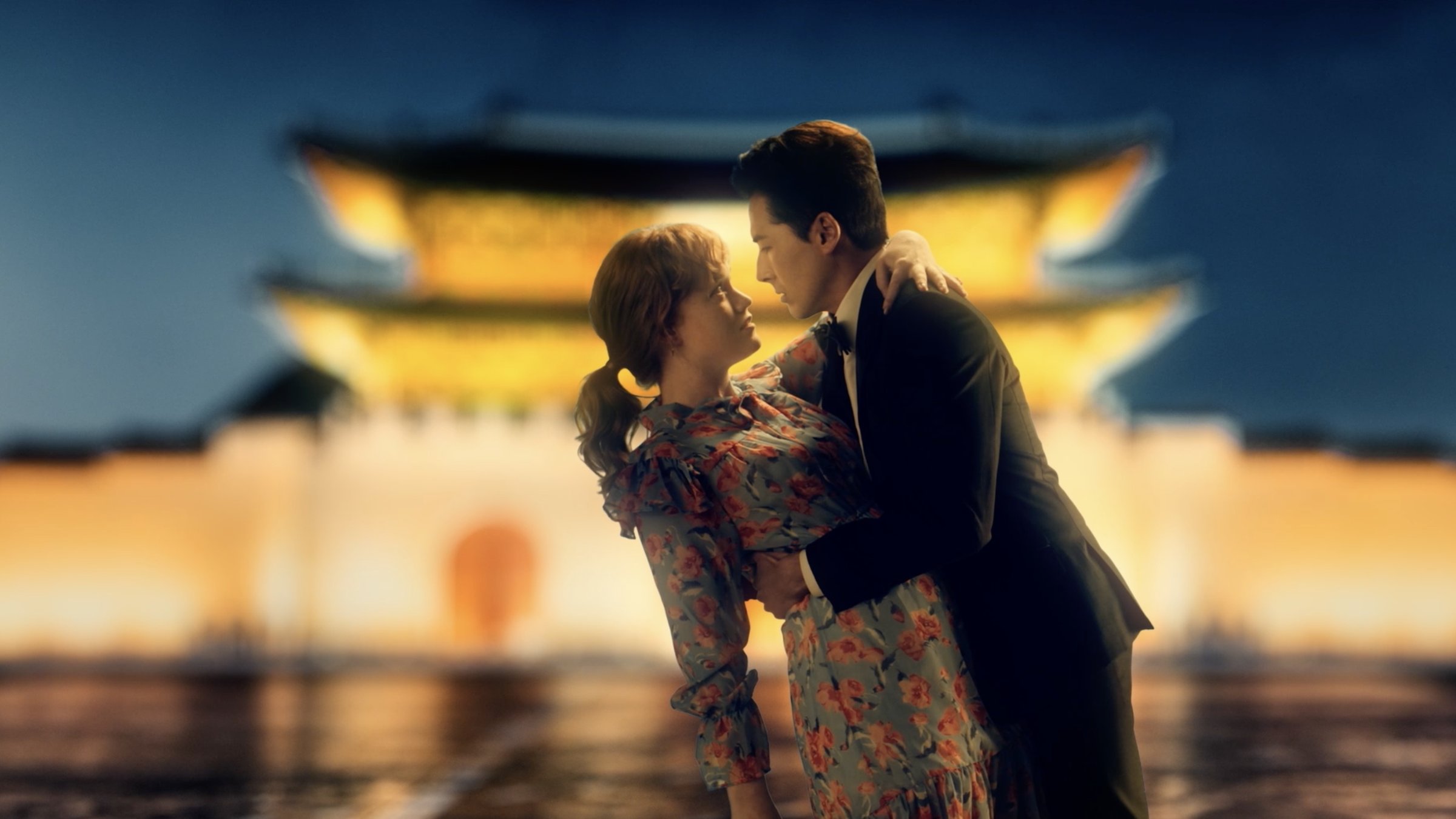Claire and Joon in a sweeping K-drama dip in front of a glowing palace gate at night