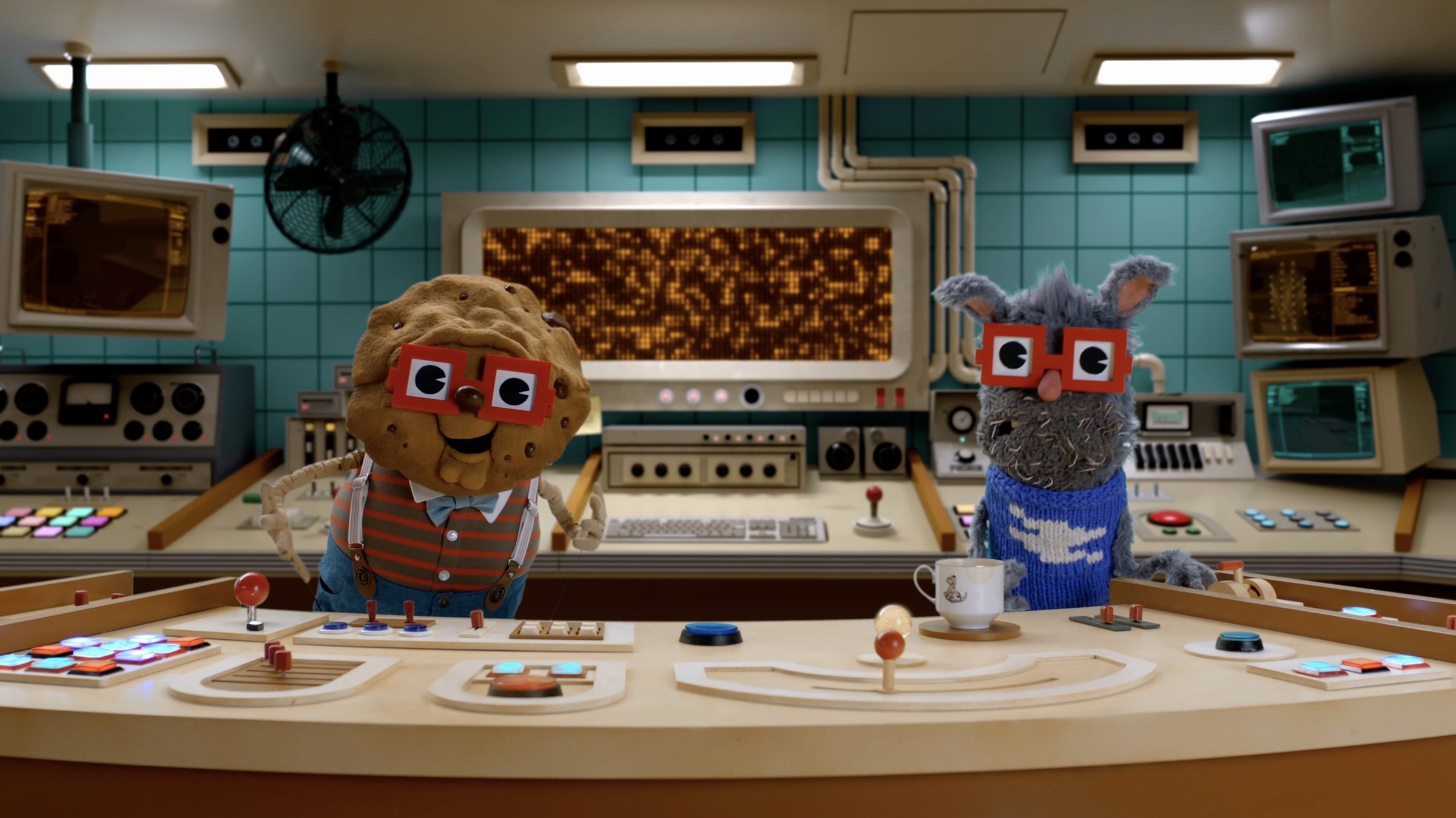We're From The Internet: Chip the cookie and Benny the rabbit, two puppets in red glasses, at a retro control console